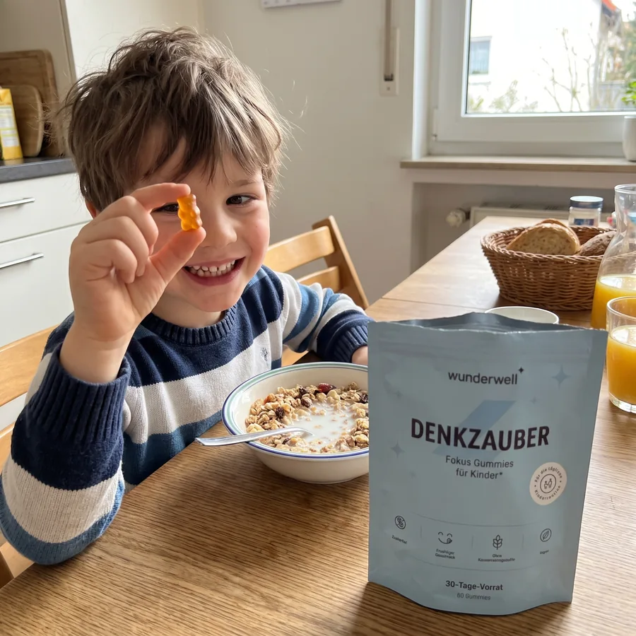 Ein Junge am Frühstückstisch mit einem orangen Gummibärchen, daneben die Denkzauber Packung