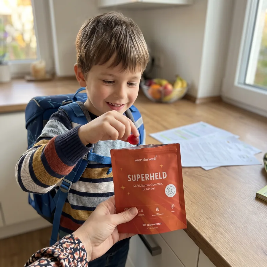 Ein Junge mit Schulranzen nimmt ein rotes Gummi aus der Superheld Packung